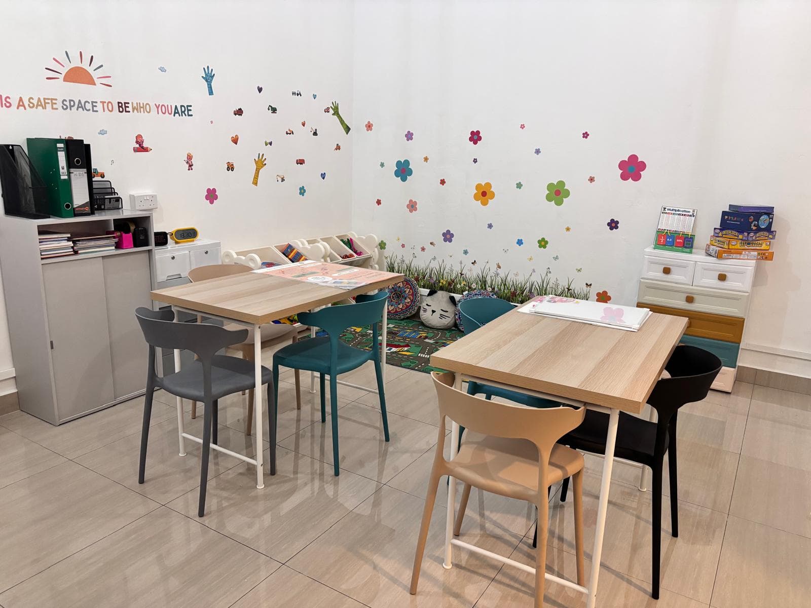 Study tables beside a flower-decal wall, board games and a play mat